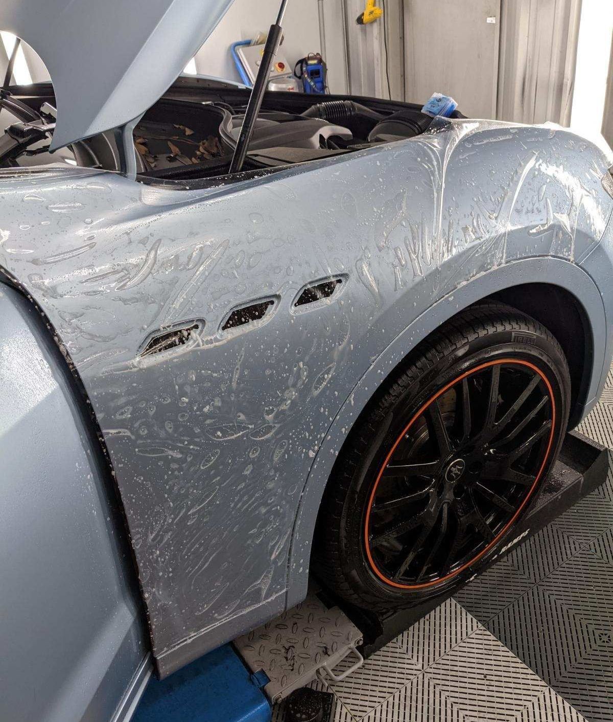A car with the hood open is sitting on a lift in a garage.