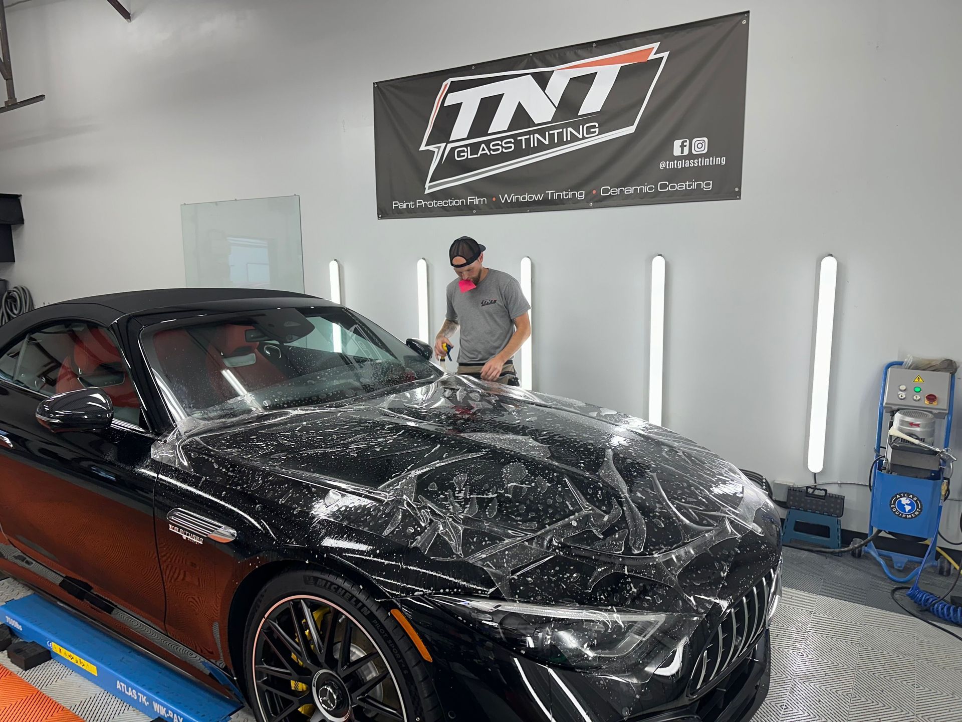 A man is wrapping a black car in plastic in a garage.