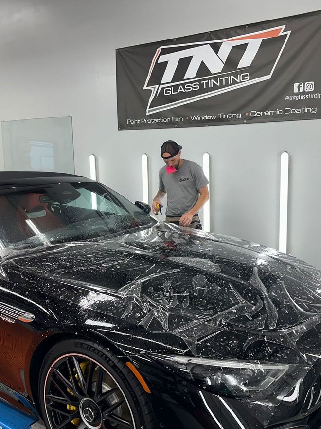 A man is covering a black car with a clear film.