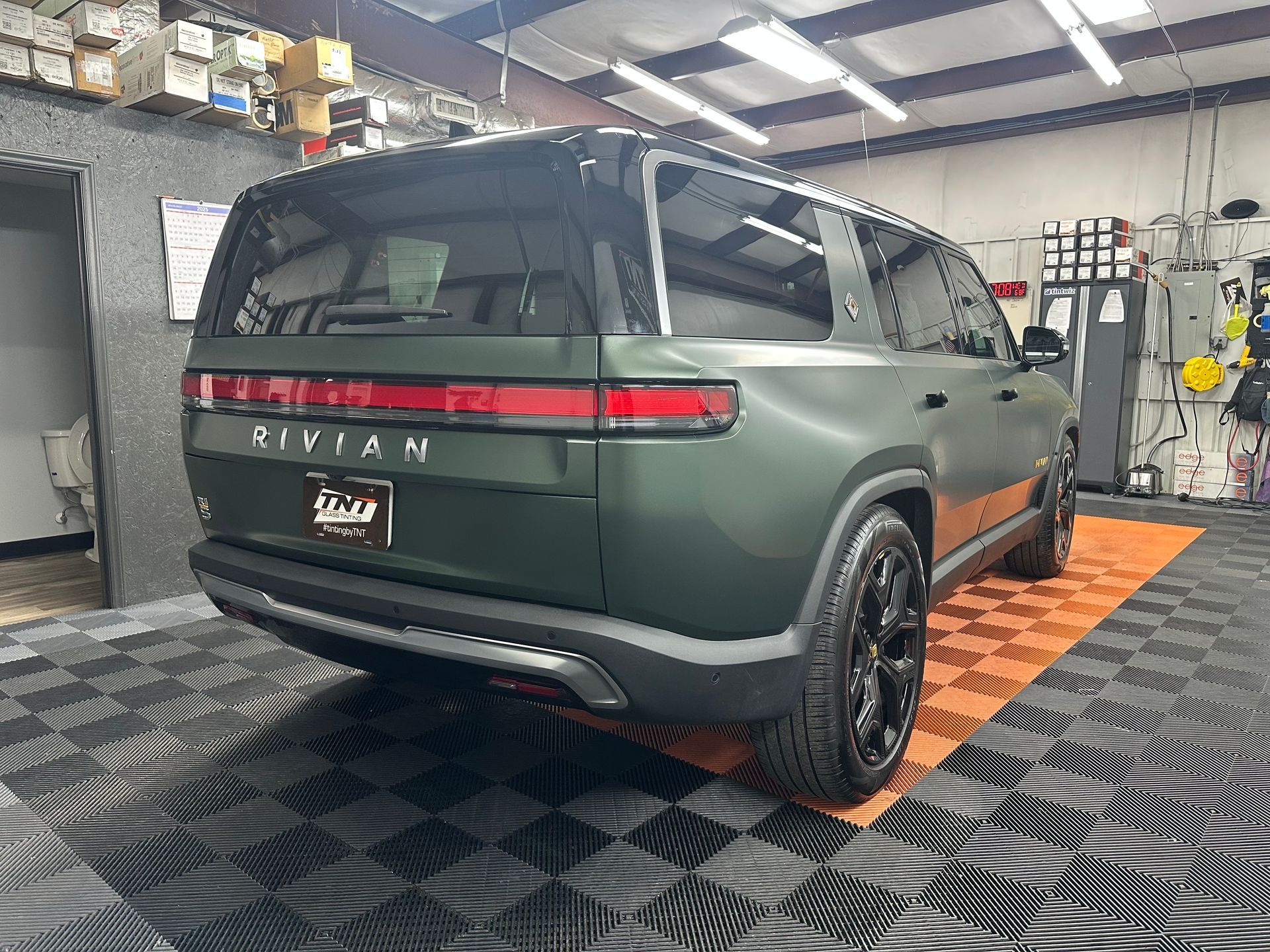 A green rivian suv is parked in a garage.