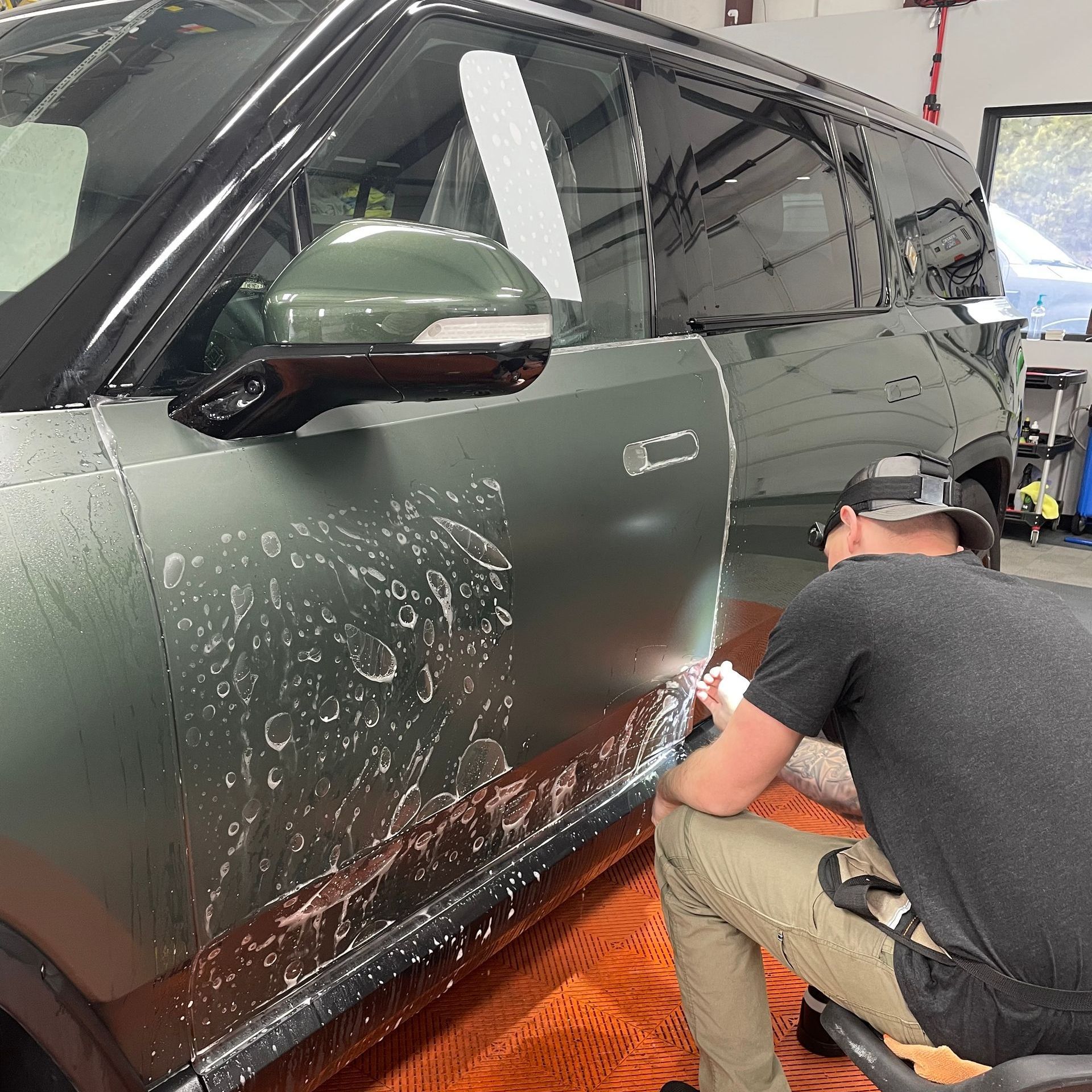 A man is kneeling down next to a car that has been wrapped in plastic.