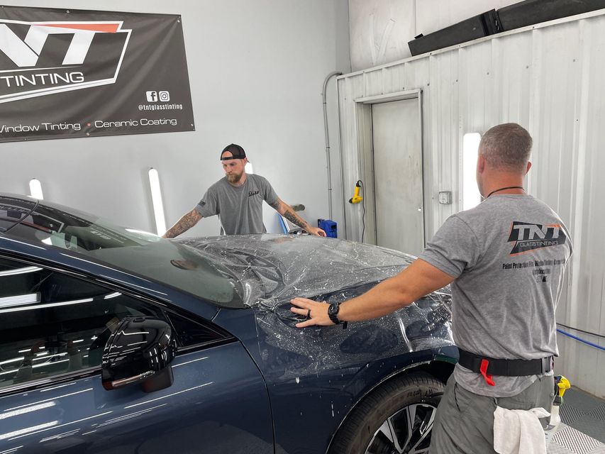 Two men are wrapping a car in plastic in a garage.