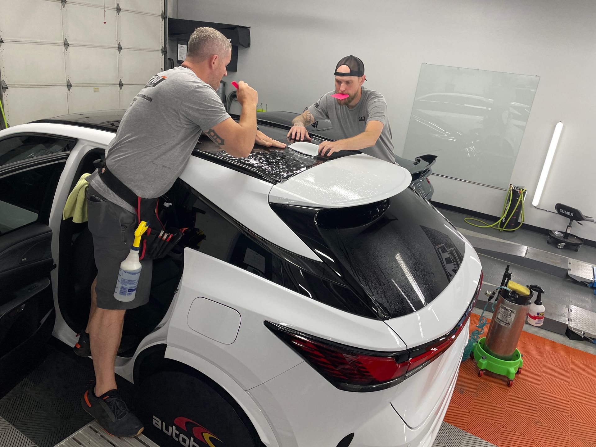 Two men are working on a white car in a garage.