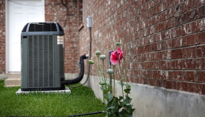 An air conditioner is sitting on the side of a brick building next to a flower.