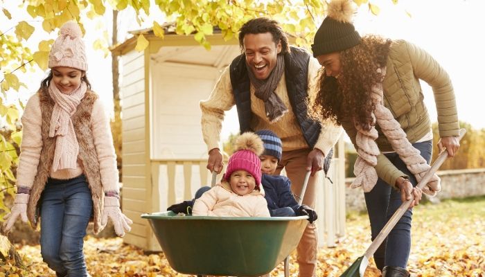 A family is pushing a child in a wheelbarrow.