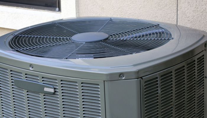 A gray air conditioner is sitting on the side of a building.