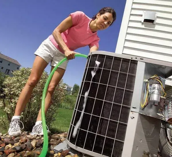A woman is cleaning an air conditioner with a green hose