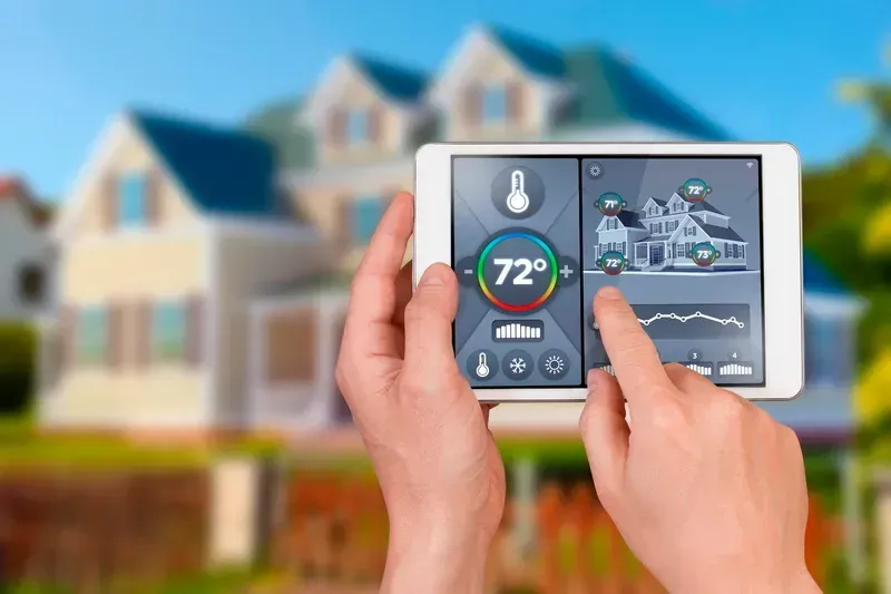A person is holding a tablet with a thermostat on it in front of a house.