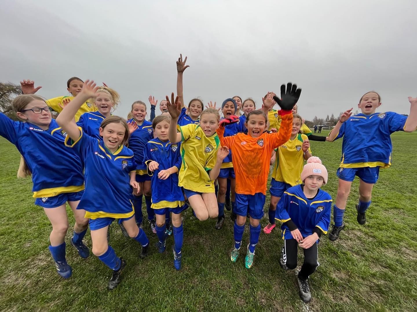 A group of young girls are jumping in the air on a soccer field.