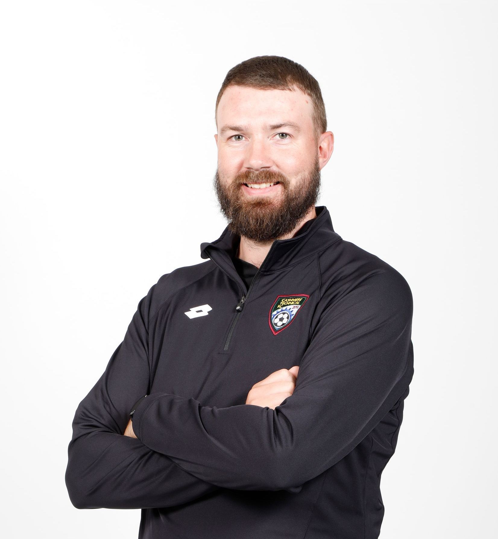 A man with a beard is wearing a black jacket with his arms crossed.