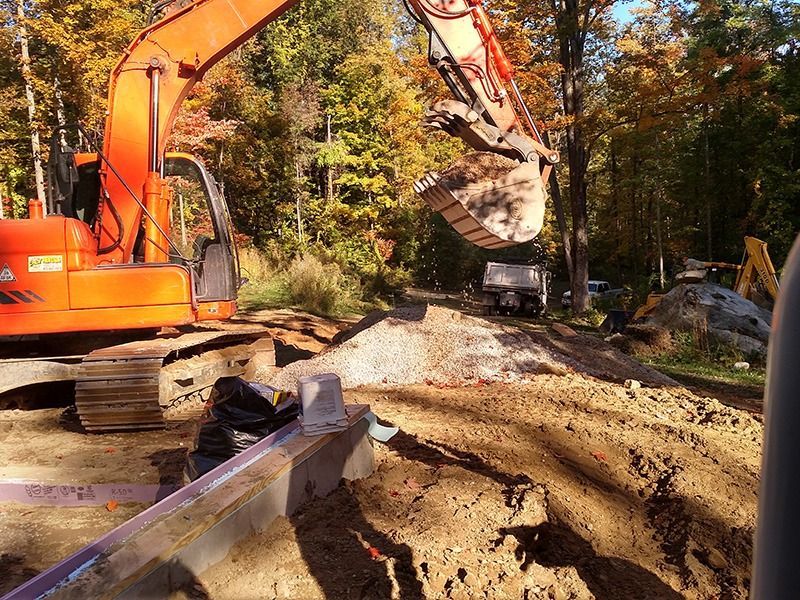 Orange excavator digging a muddy dirt road in a wooded construction area