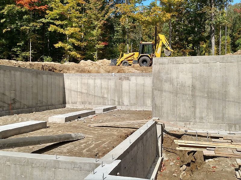 Concrete foundation under construction with excavator on a dirt slope and autumn trees in the background