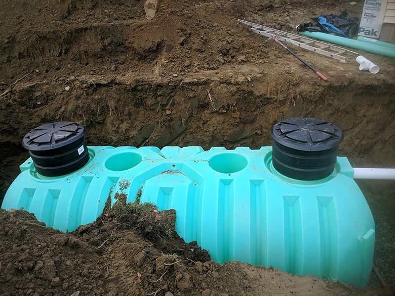 Turquoise underground water tank being installed in a trench, with black caps on top and dirt piled around it