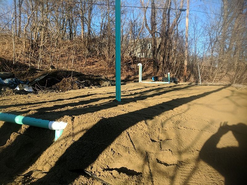 Dirt path with teal utility poles and pipes in a wooded area under clear blue sky