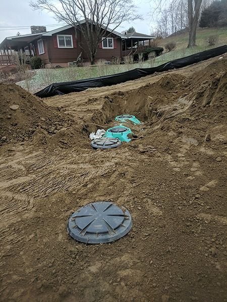 Backyard excavation with a round utility cover and exposed black pipe near a house
