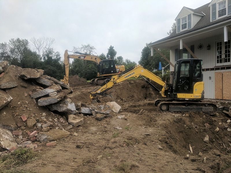 Yellow excavators clearing debris beside a house with a large pile of broken concrete and dirt.