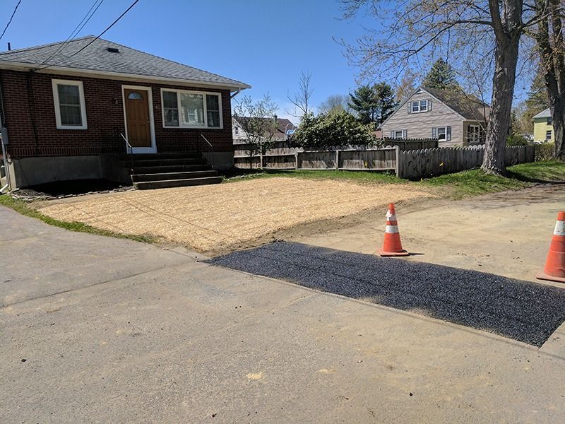 Residential lot with a small brick house, driveway, and two orange traffic cones under a clear blue sky
