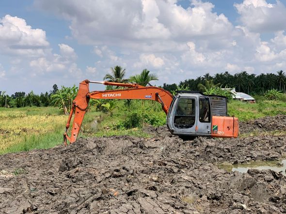 Orange excavator digging in muddy field under cloudy sky