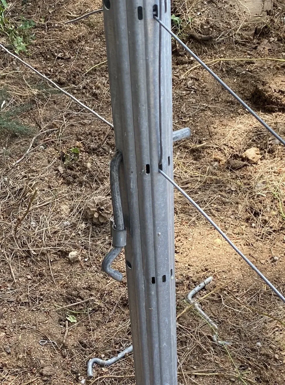 Paletto di recinzione in metallo con fili e clip metalliche in un ambiente esterno.