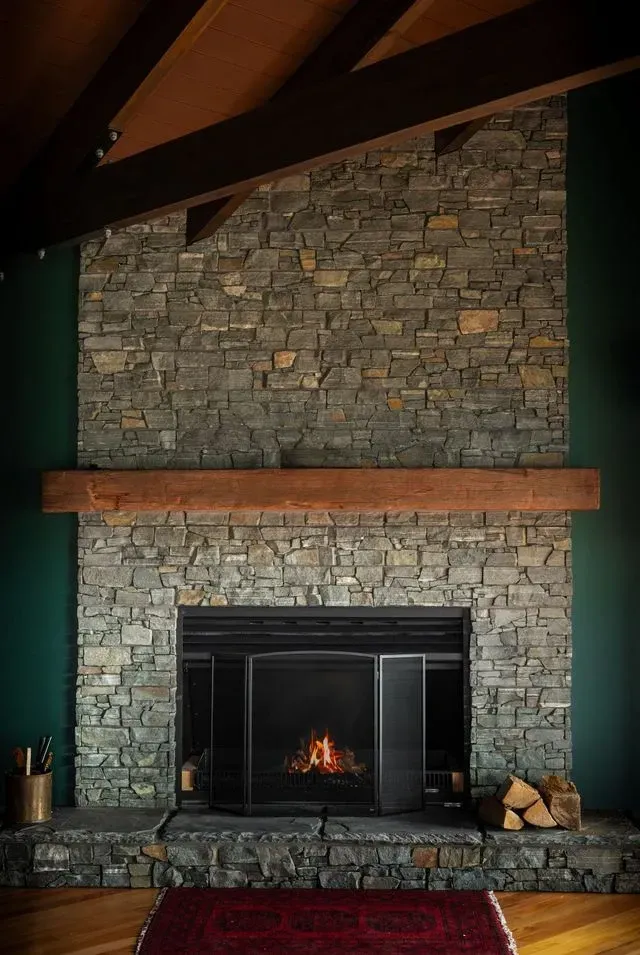 A living room with a stone fireplace and a wooden mantle.