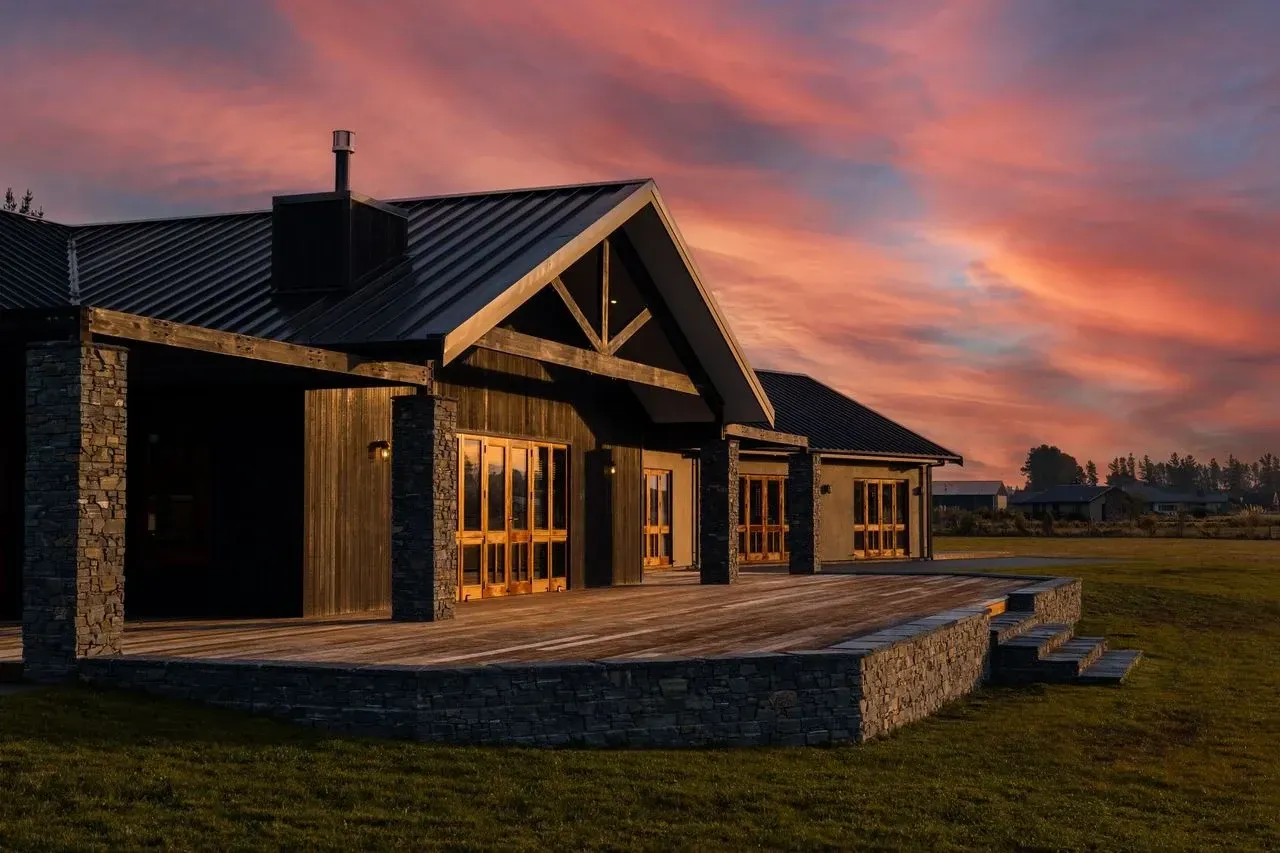 A large house with a metal roof is sitting in the middle of a grassy field at sunset.