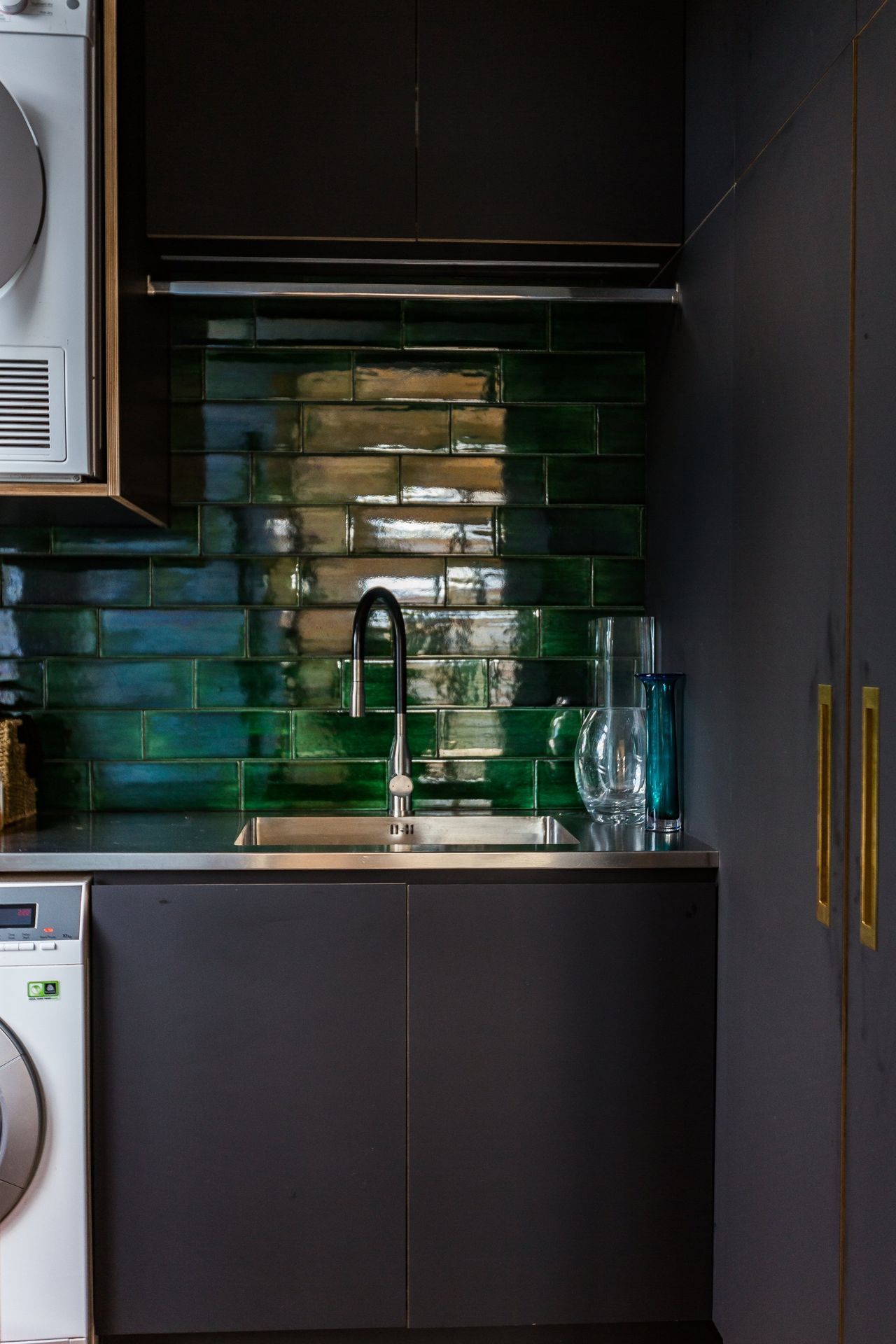 A laundry room with a washer and dryer , sink , and green tiles.