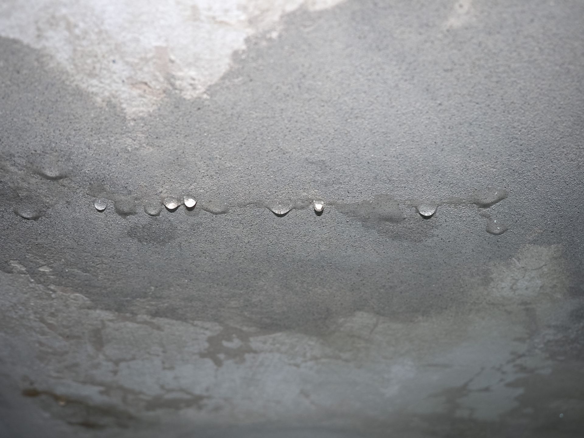 Water droplets hanging from a gray concrete surface, likely from condensation. Water droplets hanging from a gray concrete surface, likely from condensation.