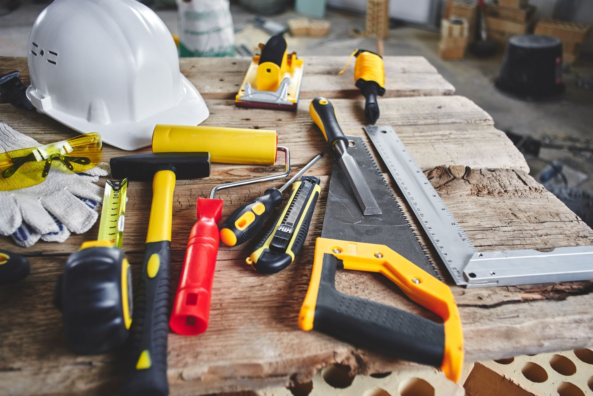 Construction tools, including a hammer, saw, and tape measure, arranged on a wooden surface.