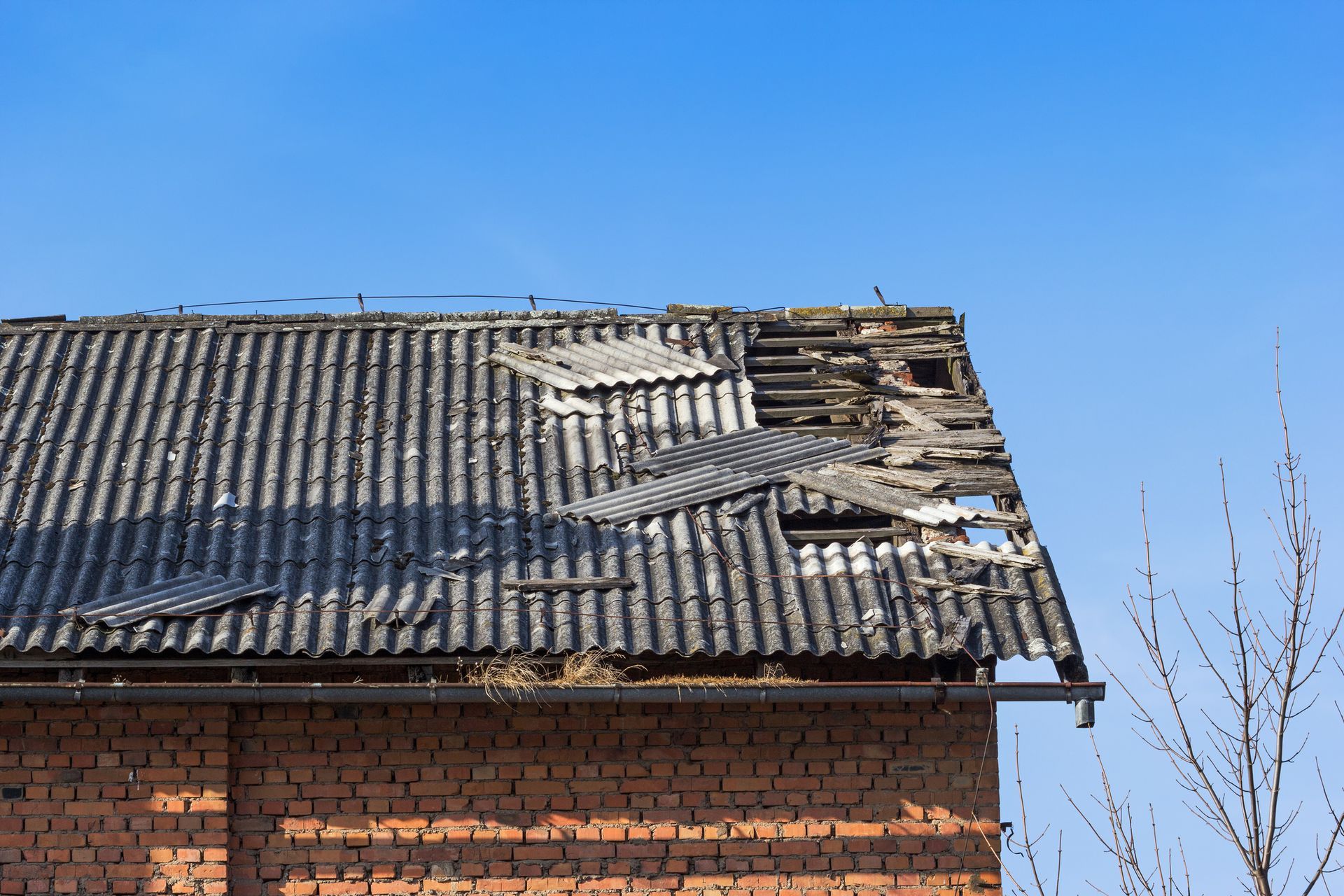 Damaged corrugated roof on a red brick building against a blue sky.