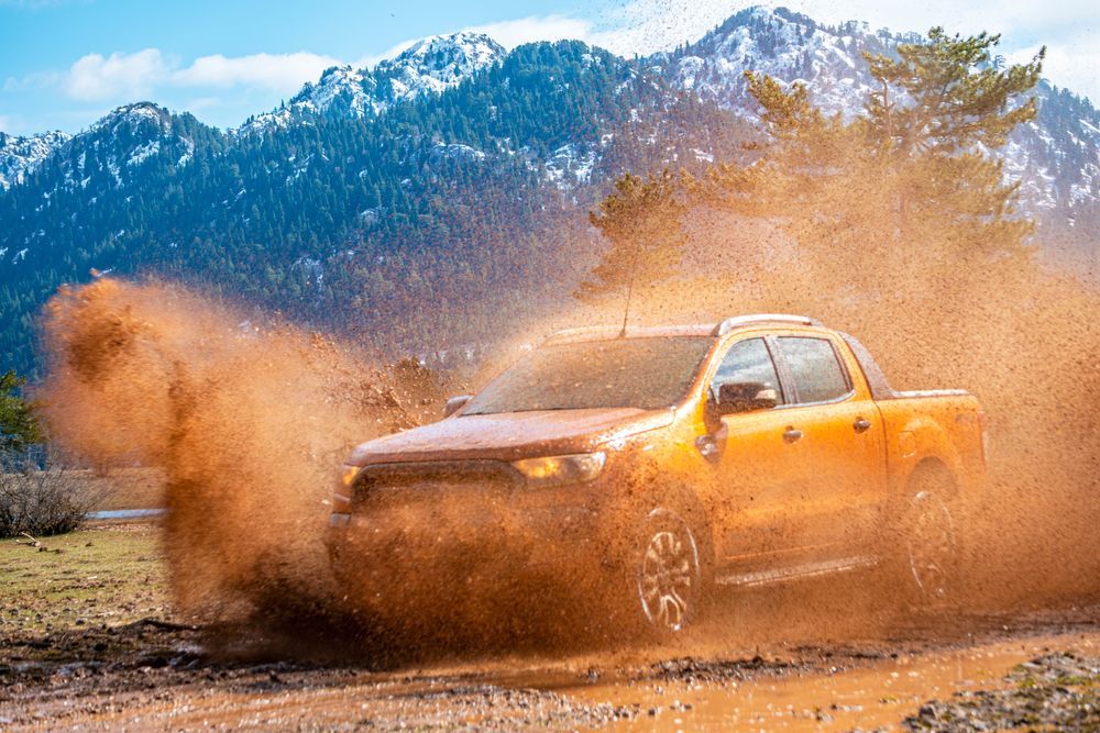Orange Pickup Truck Splashing Through Mud With Mountains in the Background — Forster Smash Repairs in Forster, NSW