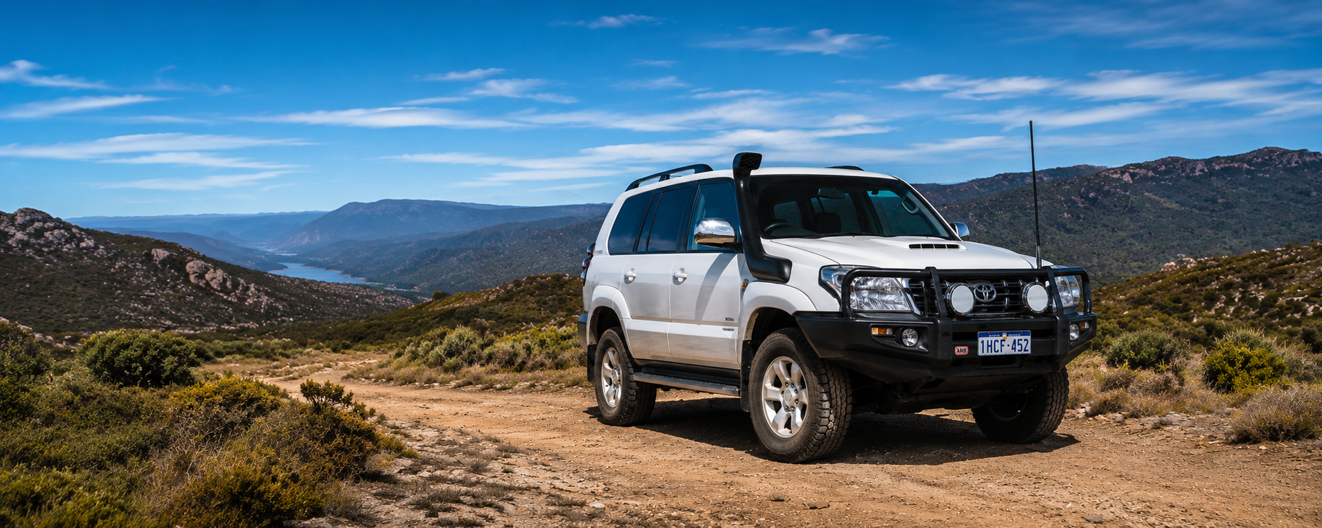 White SUV on a dirt road in a mountainous landscape under a clear blue sky
