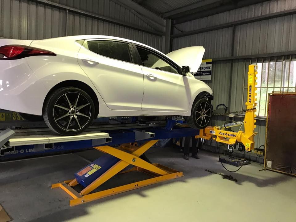 White Sedan Raised on a Yellow Scissor Lift in an Auto Repair Shop, Hood Open — Forster Smash Repairs in Forster, NSW