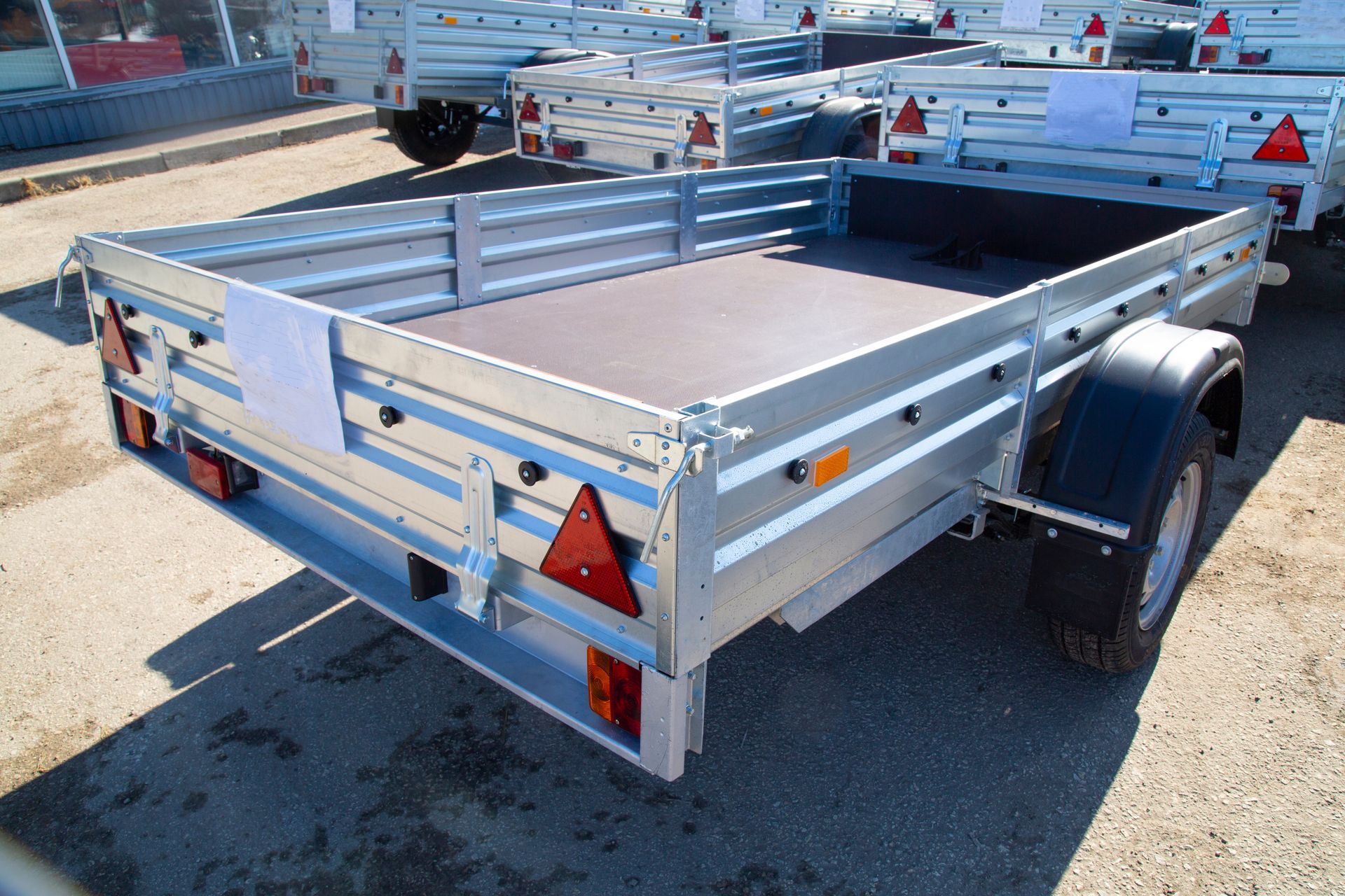 Small silver utility trailer with wooden floor and red reflectors parked in a lot.