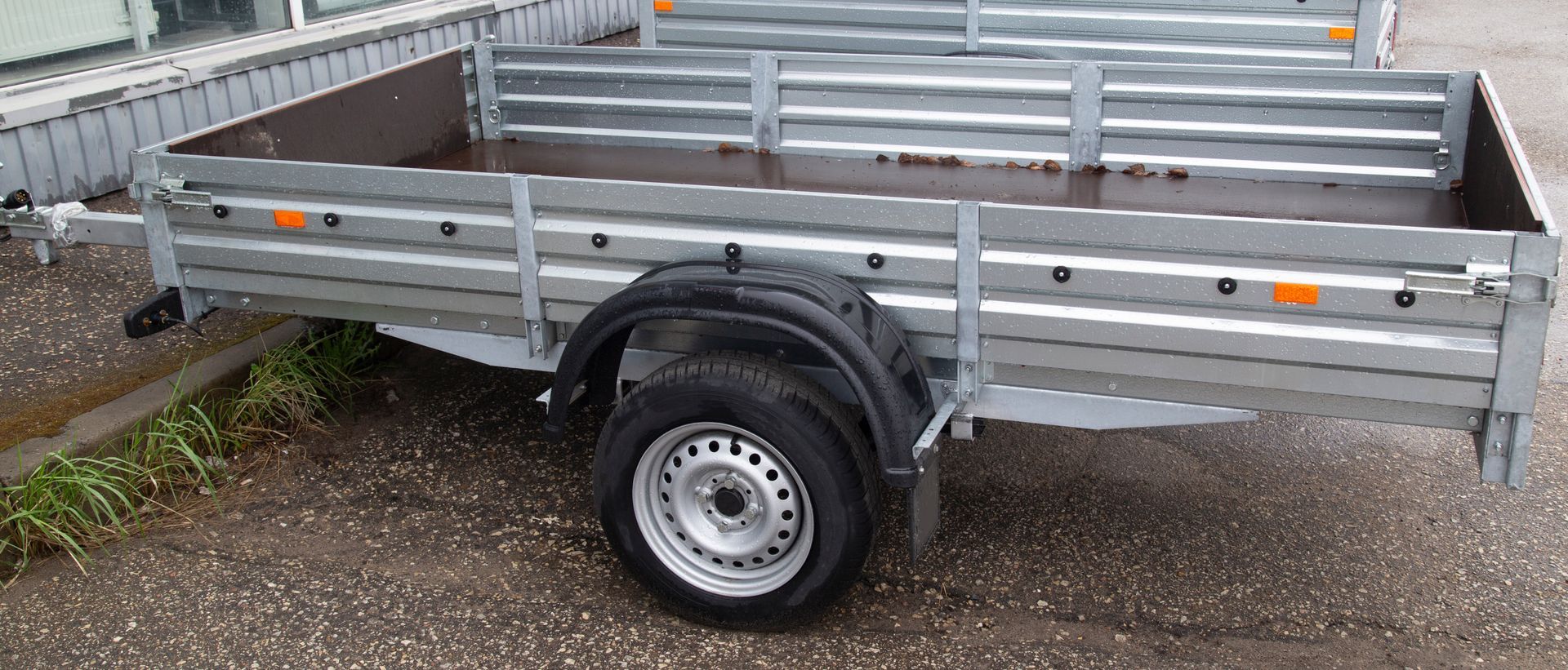 Gray metal utility trailer with one wheel and raised side panels, parked on pavement.