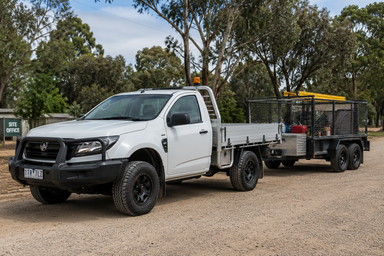 White utility truck towing a trailer with equipment on a gravel road, trees in the background