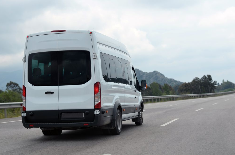 White Passenger Van Driving on a Highway Beside Mountains Under a Cloudy Sky — Forster Smash Repairs in Forster, NSW