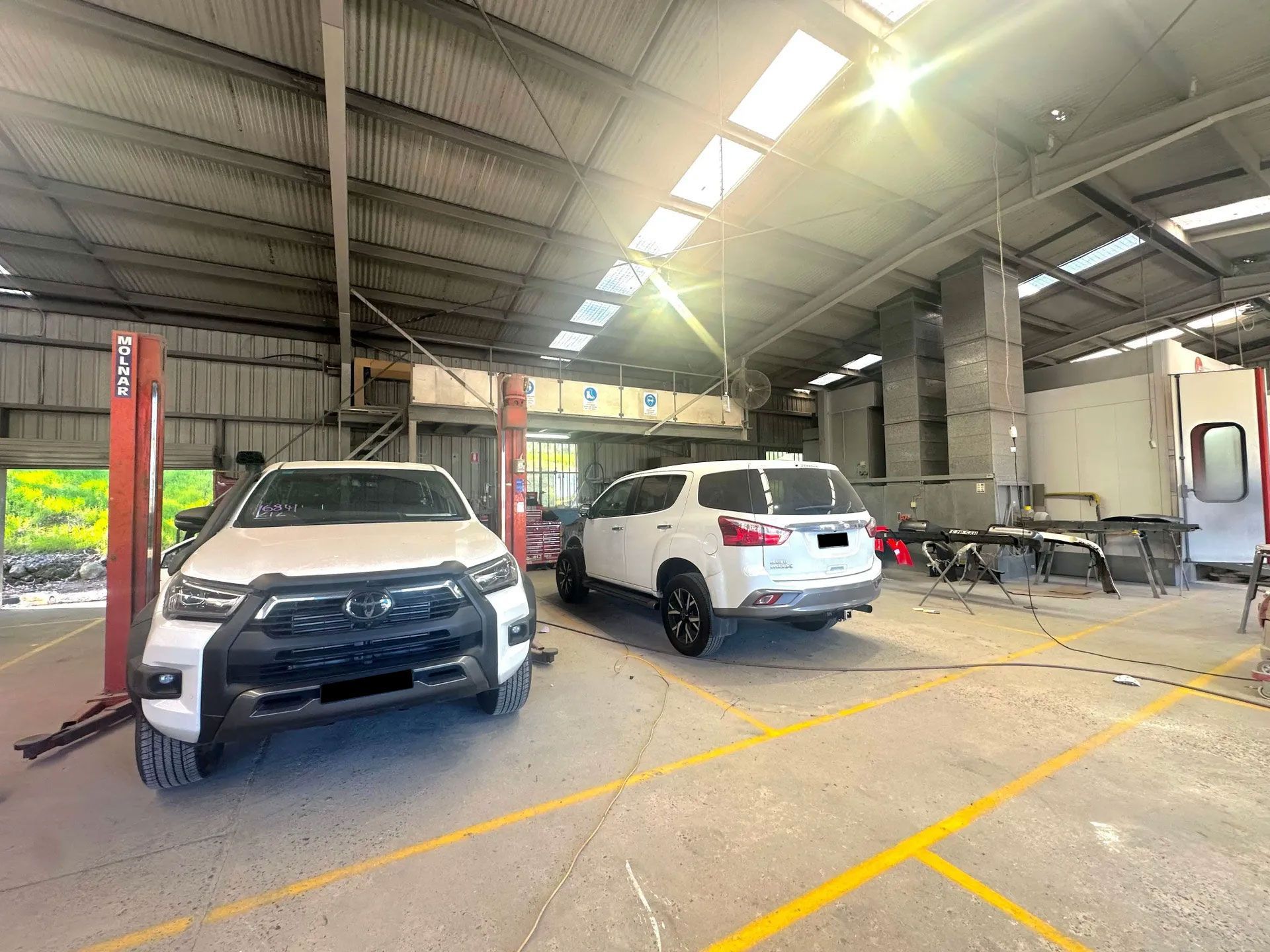Cars Parked in a Service Garage With Overhead Lights and a Lift — Forster Smash Repairs in Forster, NSW