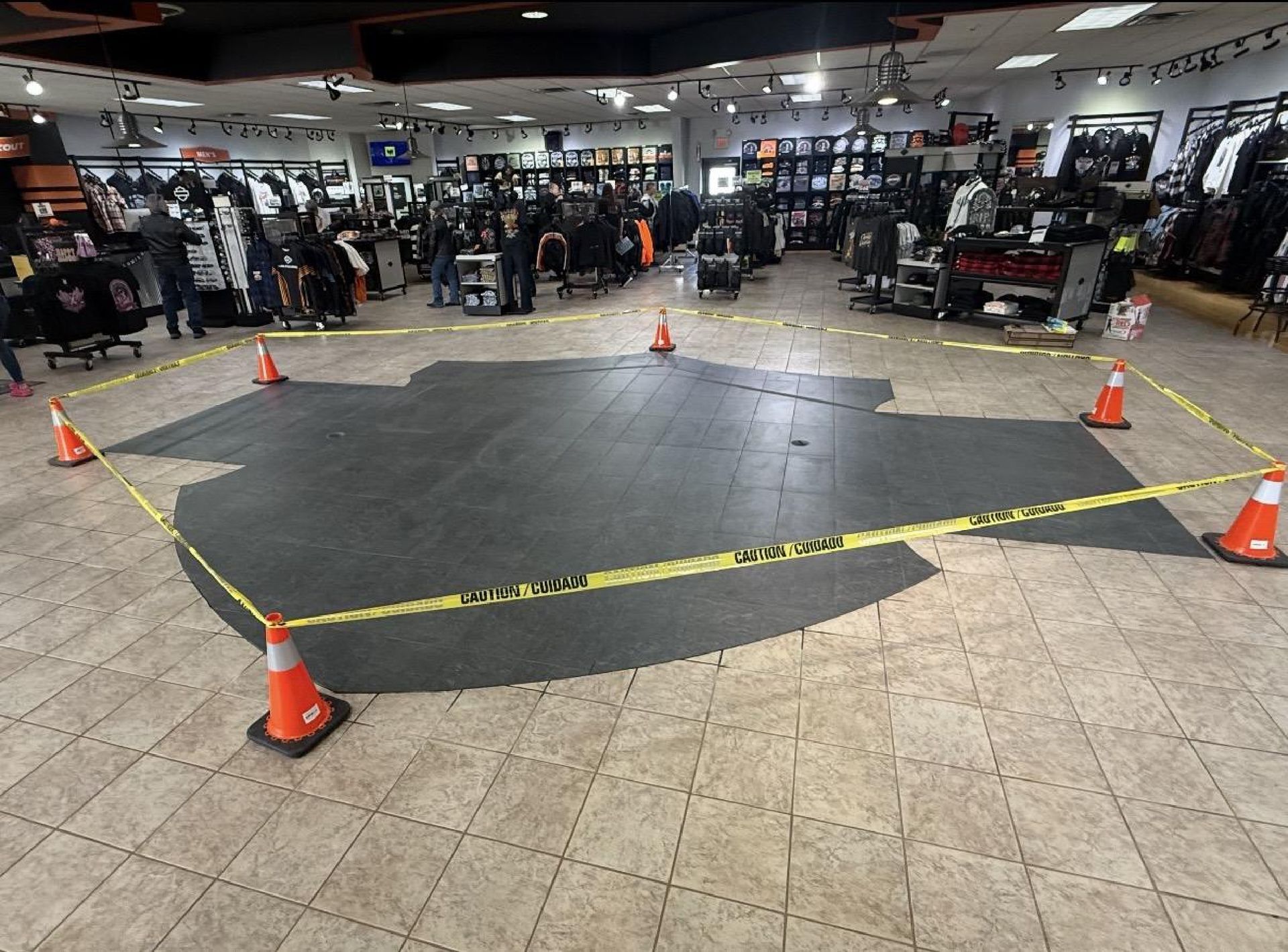 A dark, shield-shaped floor mat in a retail store, cordoned off by yellow caution tape and orange traffic cones.
