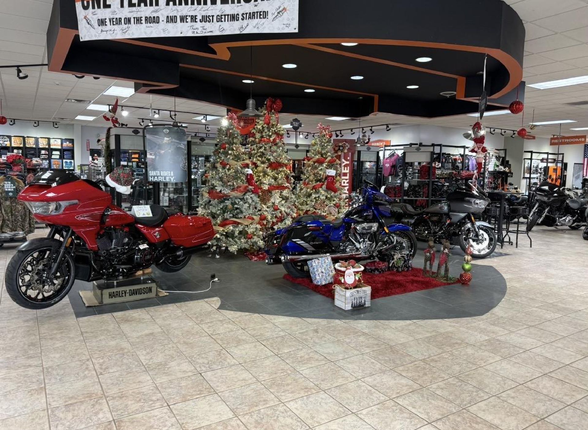 A dealership showroom displays a red and a blue motorcycle parked near decorated Christmas trees and gift boxes.