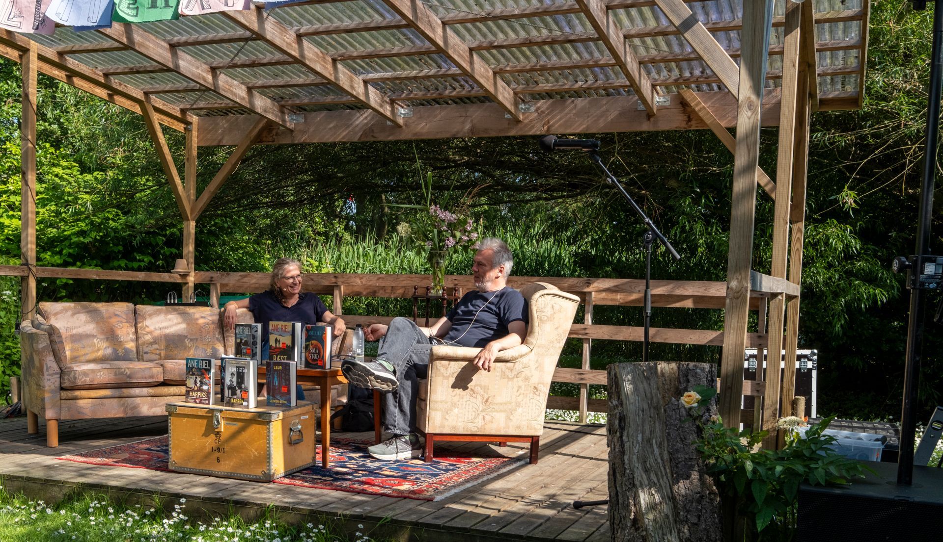 To mænd sidder på stole under en pergola.