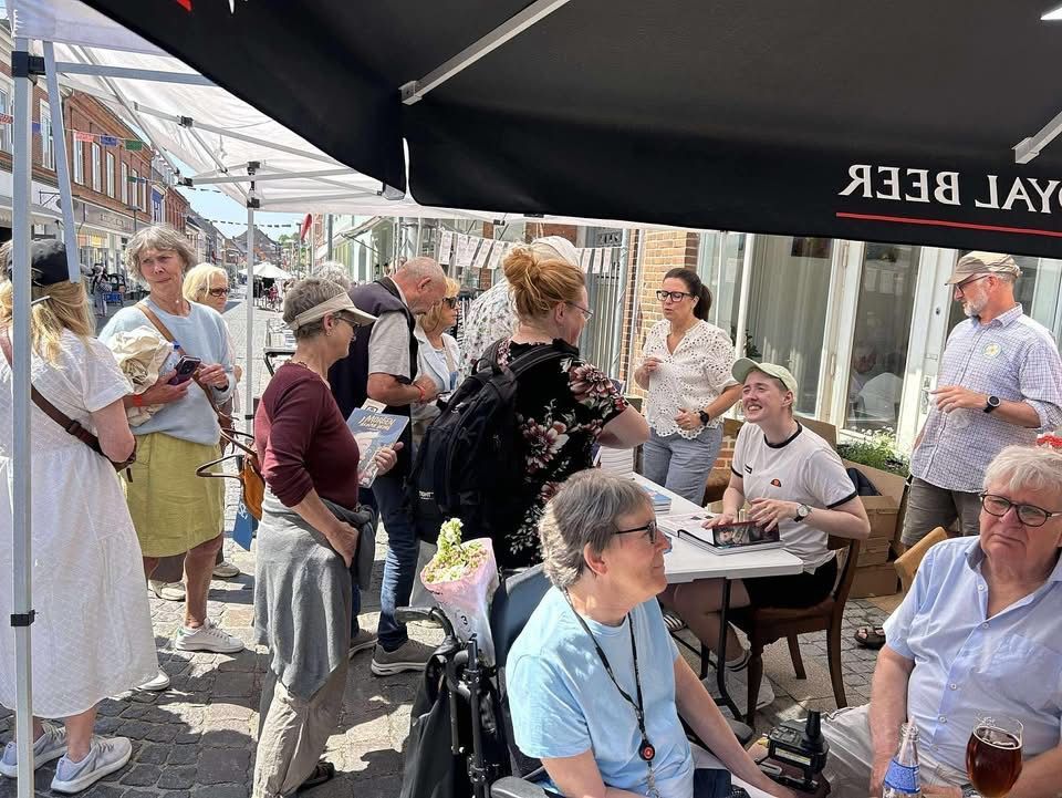En gruppe mennesker står omkring et bord under en parasol.