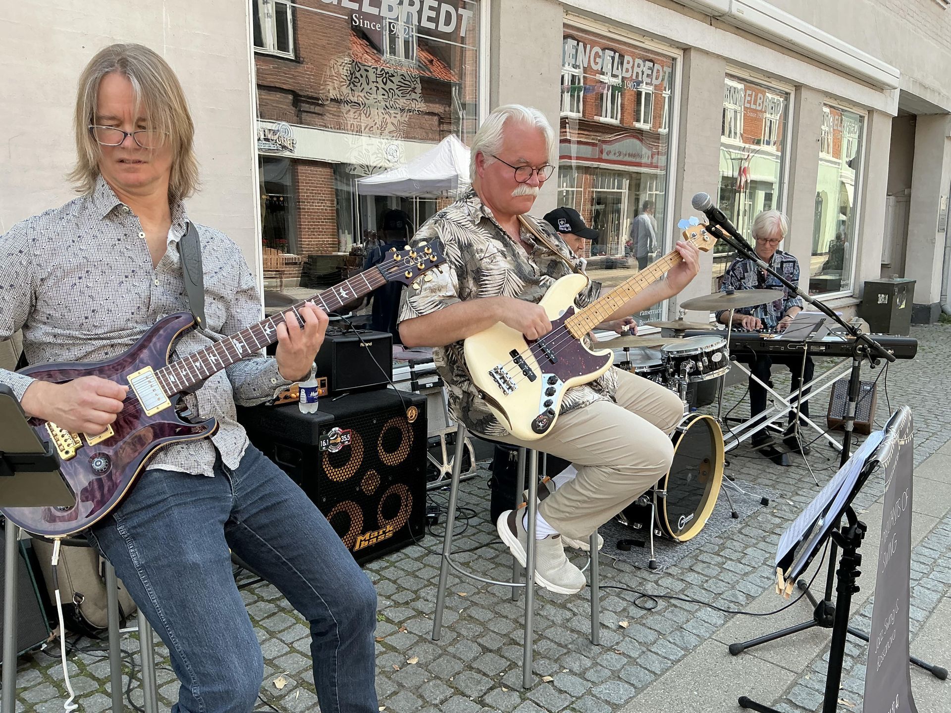 En gruppe mænd spiller guitar og trommer på en brostensbelagt gade.