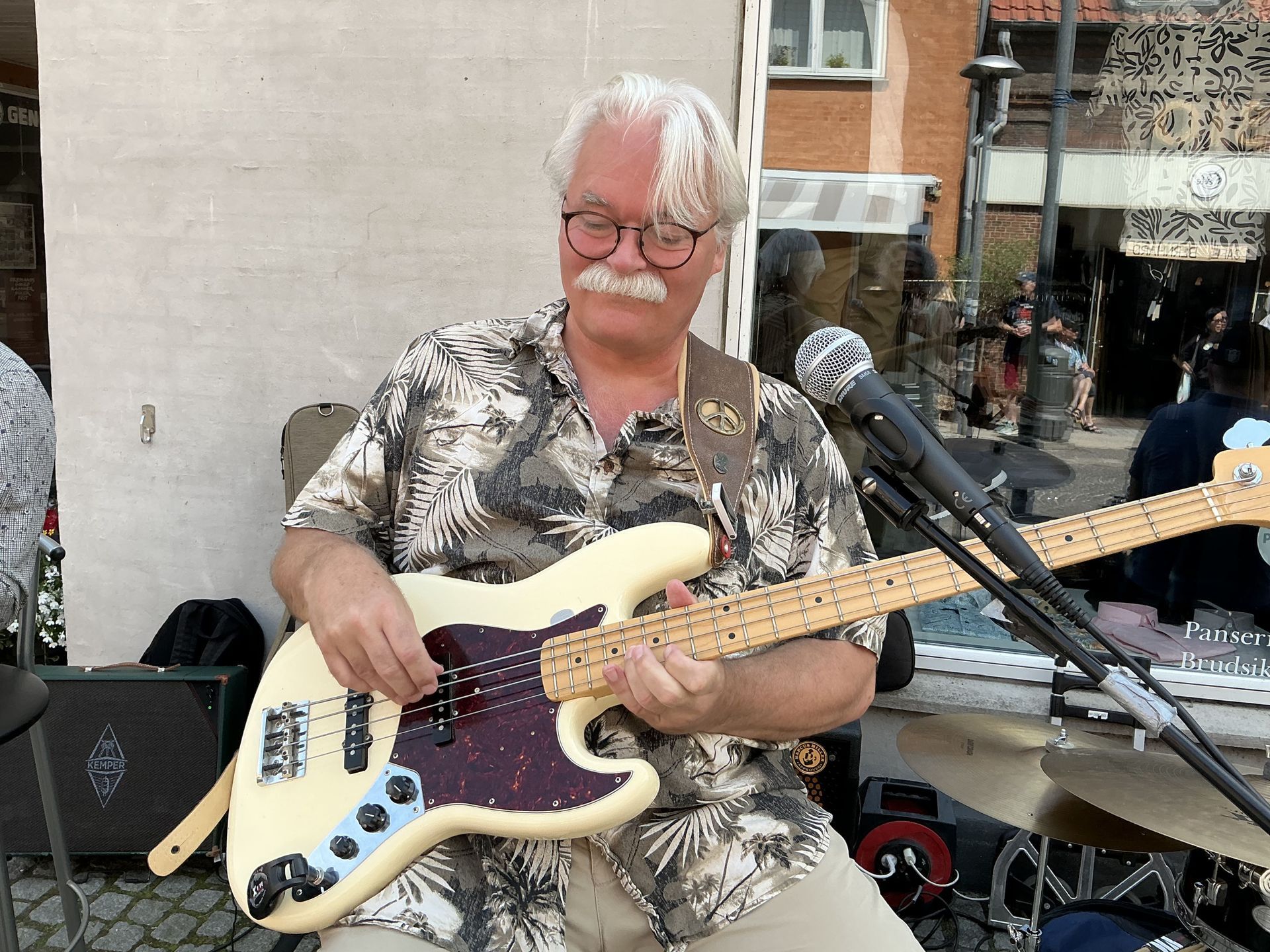 En mand med briller og overskæg spiller guitar foran en mikrofon.