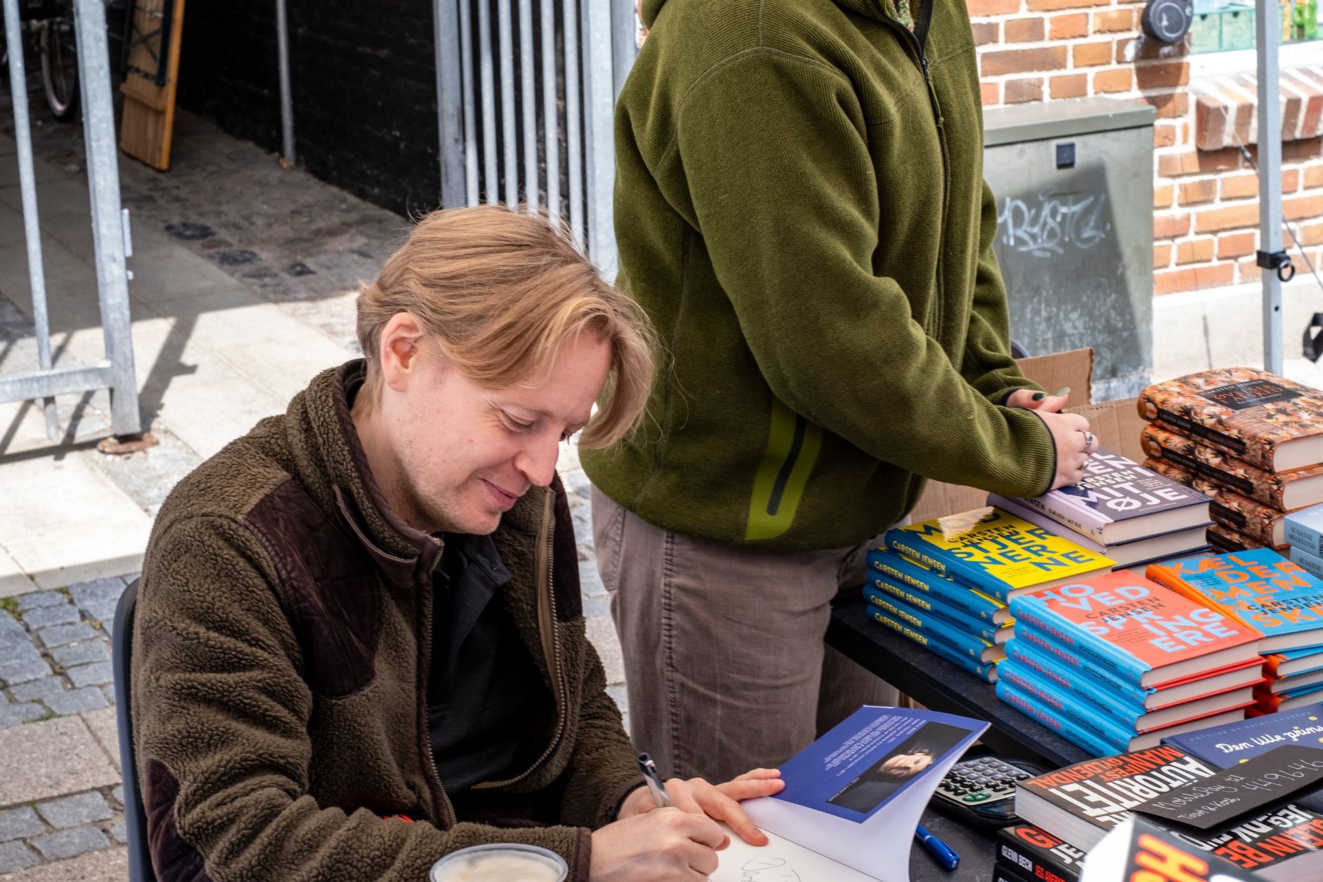 En mand sidder ved et bord og signerer en bog.