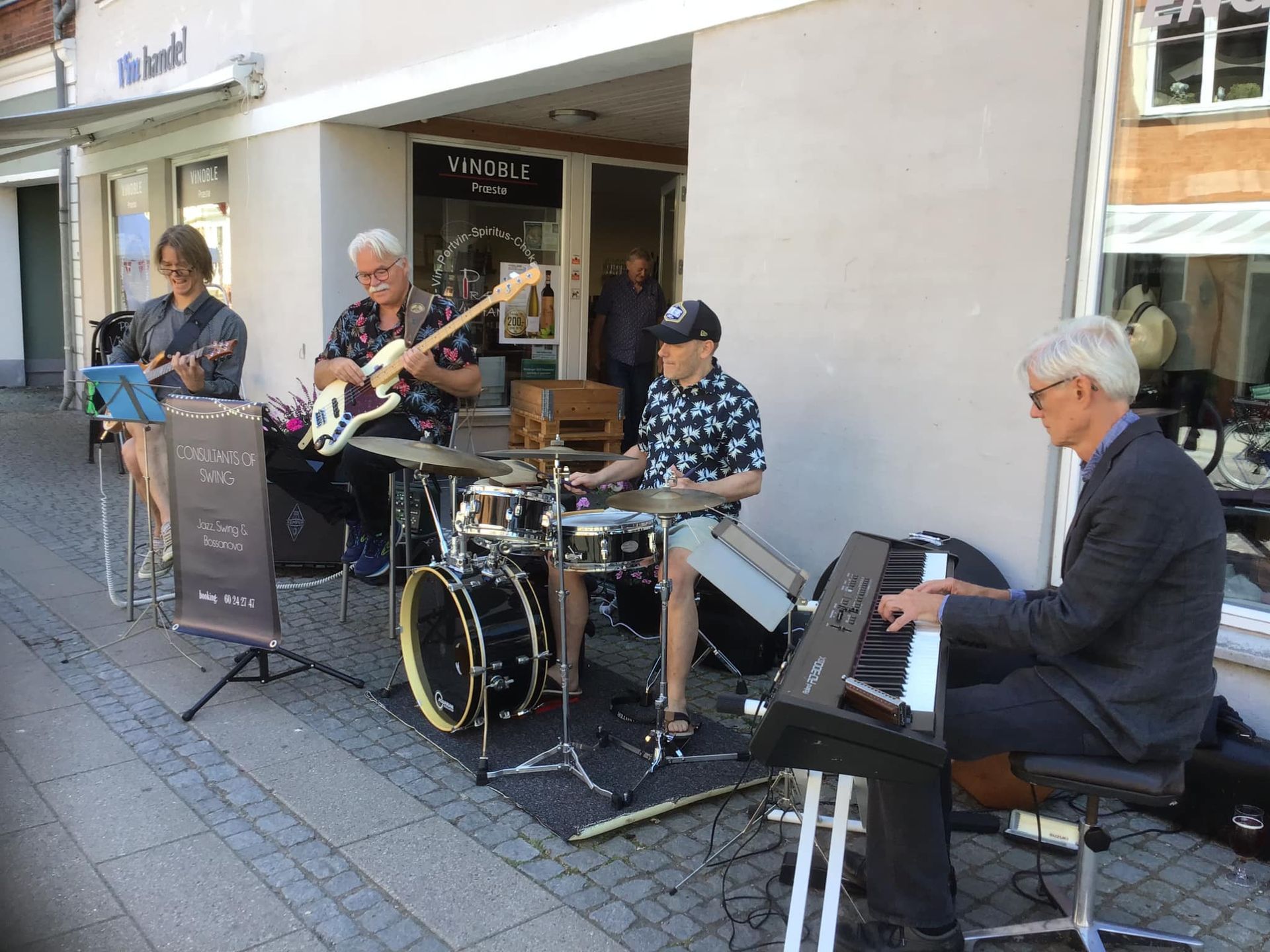 En gruppe mænd spiller instrumenter på et fortov foran en bygning.