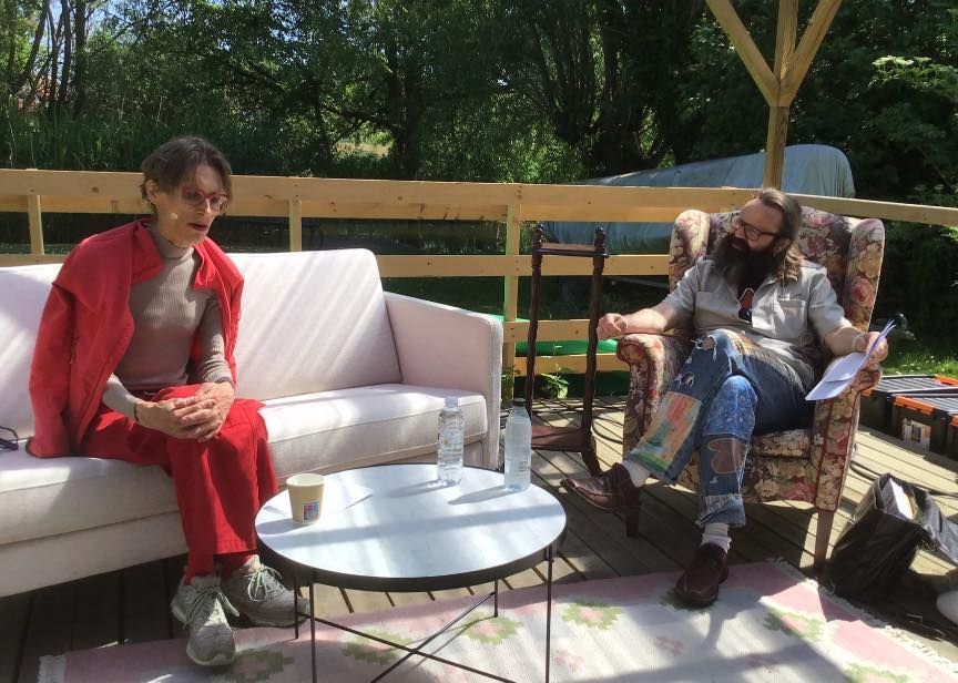 To personer sidder på en sofa og en stol på et dæk.