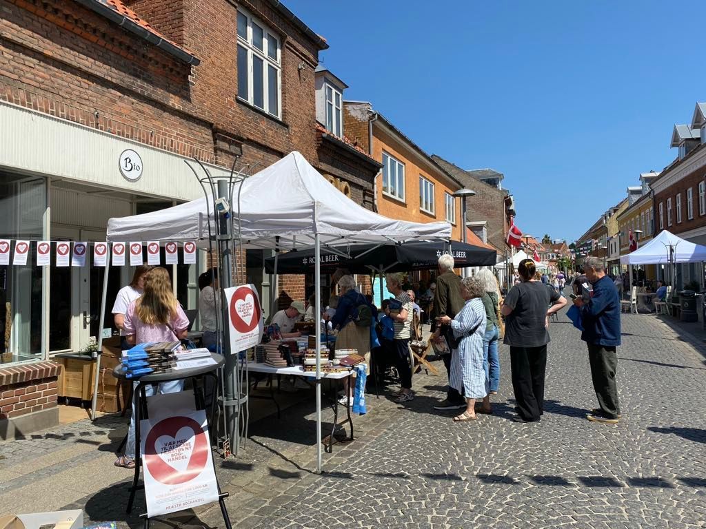 En gruppe mennesker står omkring telte på en brostensbelagt gade.