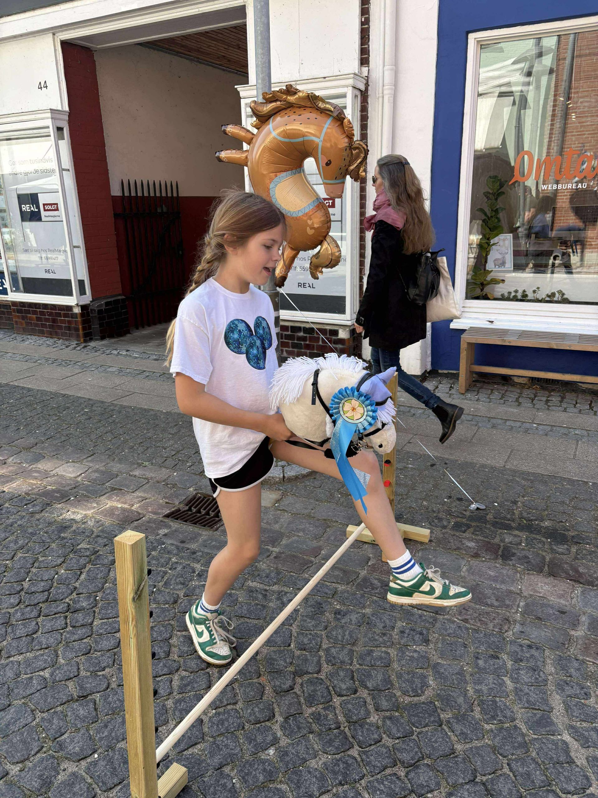 En lille pige leger med en tøjhest på en brostensbelagt gade.