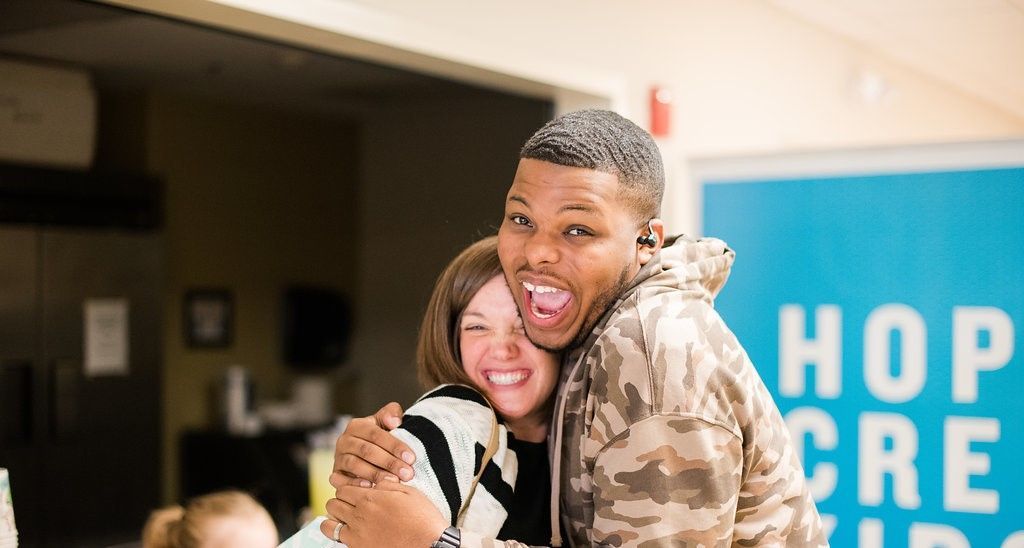 A man and a woman are hugging each other in a hallway in front of the Hope Creek Kids sign