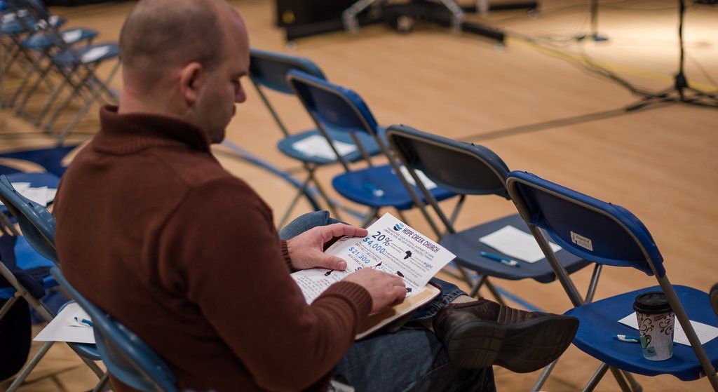 A man is sitting in a row of folding chairs looking at a piece of paper.